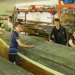 Leaders and crew members prepare skiff for varnishing and painting